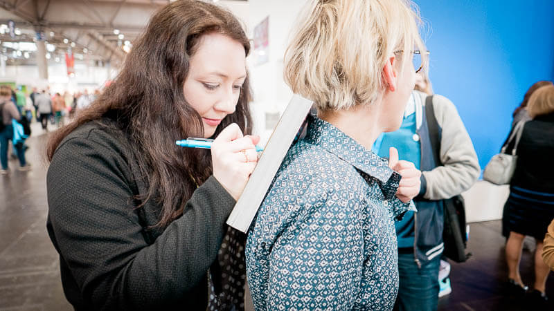 Leipziger Buchmesse 2017 Anna Pfeffer beim Signieren auf dem Rücken von Claudia Winter